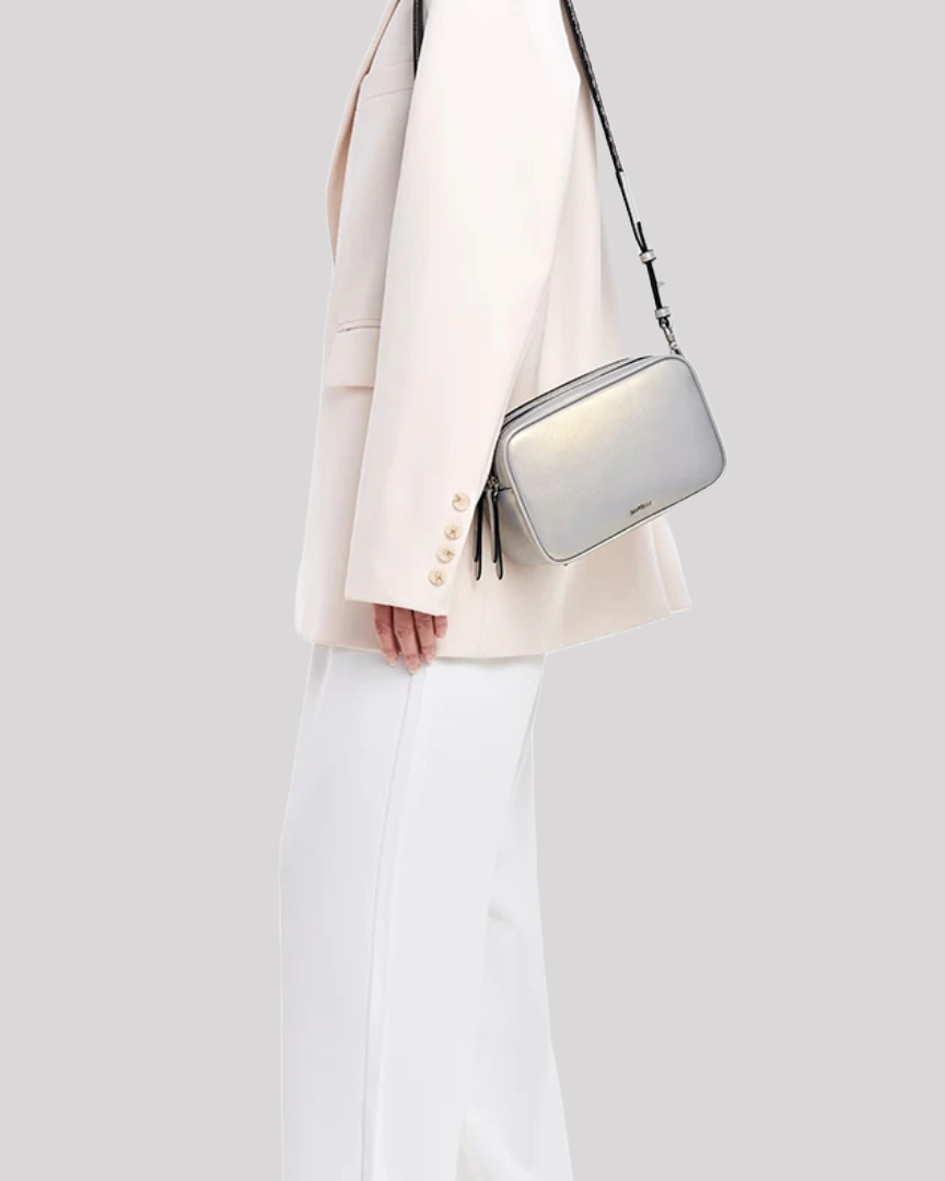 Metallic silver crossbody bag by Bafelli styled over the shoulder by model in white outfit