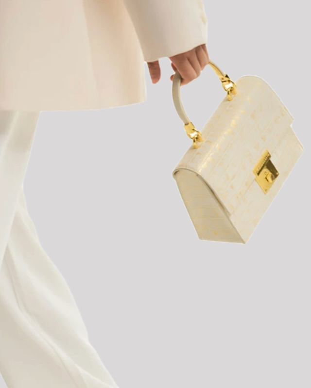Model carrying white croc-embossed top handle bag by Bafelli with gold lock, structured silhouette, and elegant handle