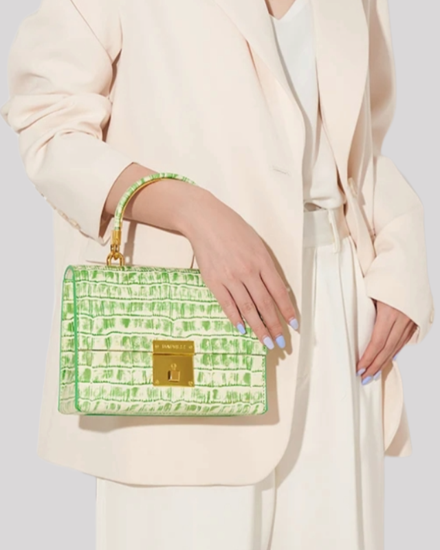 Woman holding white and green croc-embossed top handle bag by Bafelli with gold hardware and structured silhouette