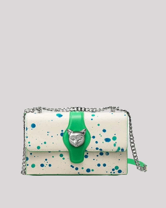 Front view of white crossbody bag with green leather strap, blue and green paint splatter design, silver cat head clasp, and chain shoulder strap
