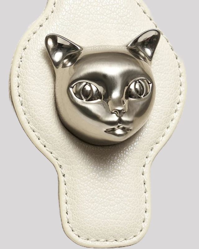 Detailed close-up of metallic silver cat head clasp on white leather shoulder bag