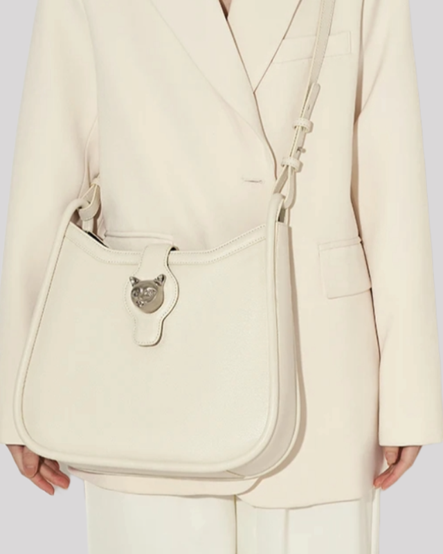 White leather shoulder bag with silver cat head clasp worn crossbody by model in white blazer
