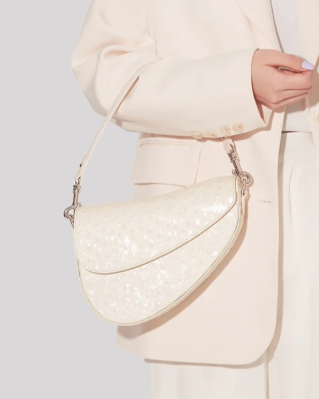 White ostrich-embossed asymmetric shoulder bag by Bafelli held by model wearing cream blazer and pants