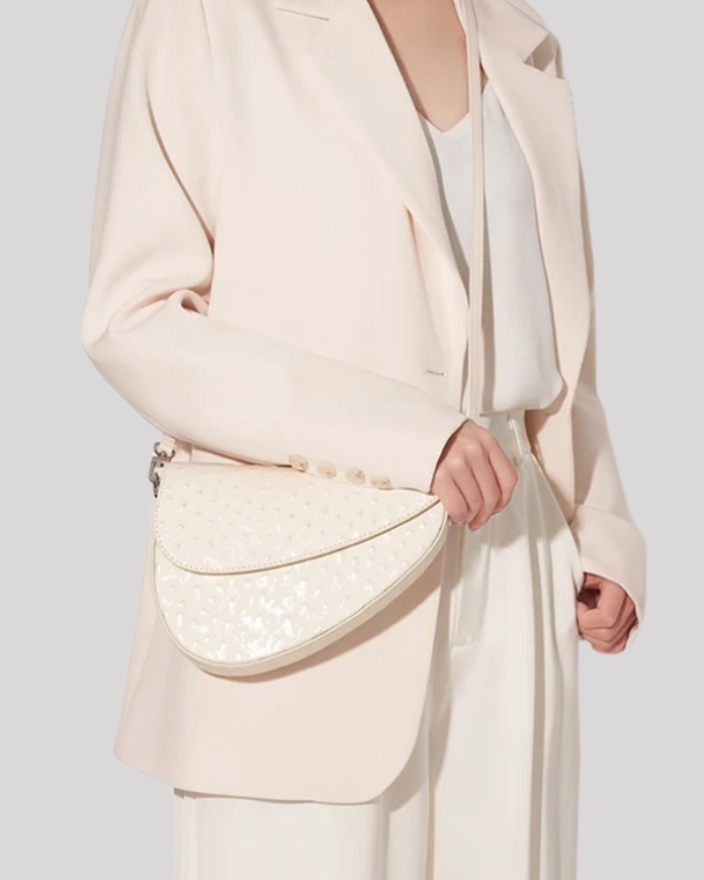 Model wearing cream suit carrying white ostrich-embossed asymmetric shoulder bag by Bafelli on shoulder