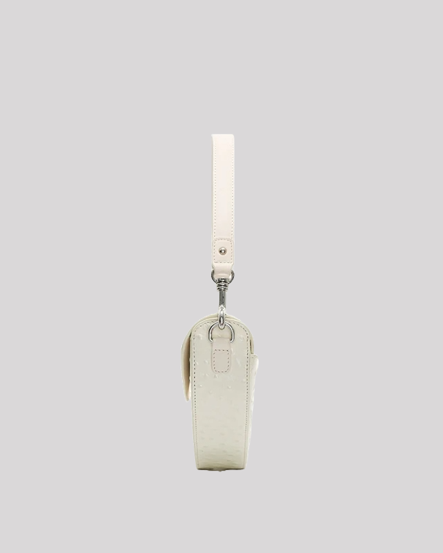 Slim side profile of white ostrich-embossed asymmetric shoulder bag by Bafelli with detachable strap