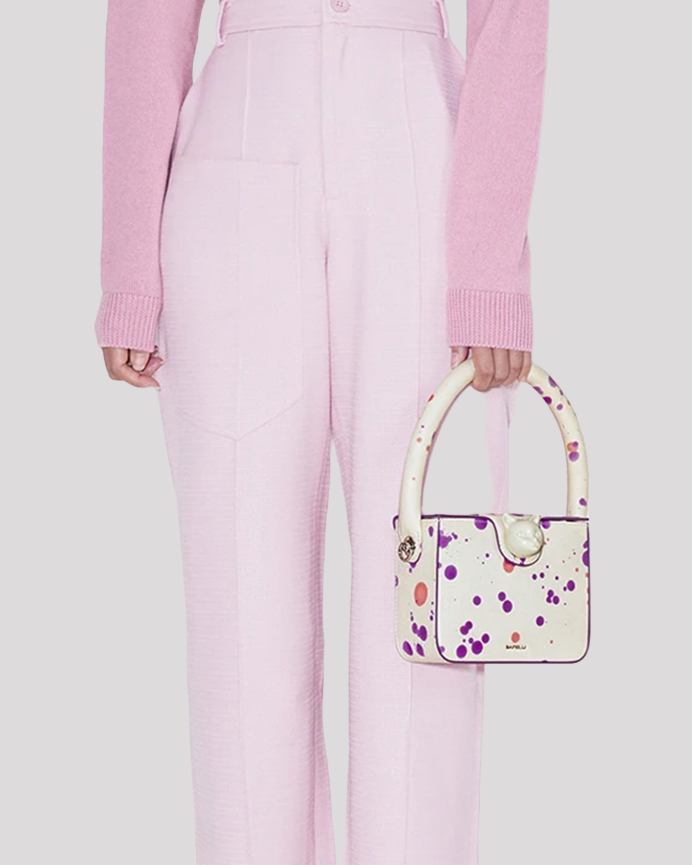 Woman holding white mini bag by Bafelli with purple splatter design – pastel outfit view