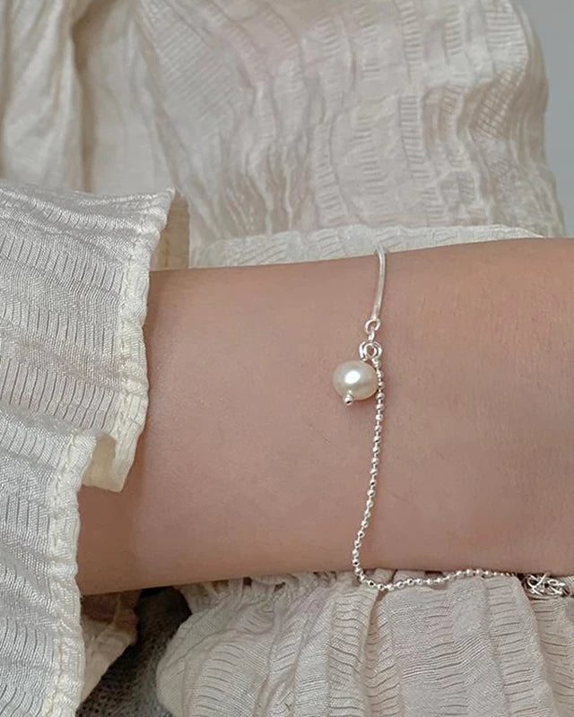 Close-up of women’s silver bracelet with pearl pendant – delicate minimalist jewelry piece