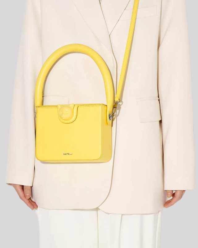 Model wearing yellow Bafelli cat-handle bag over the shoulder with structured square design
