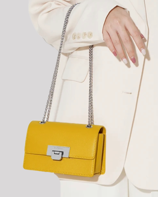 Yellow mini crossbody bag by Bafelli carried by hand with long silver chain strap